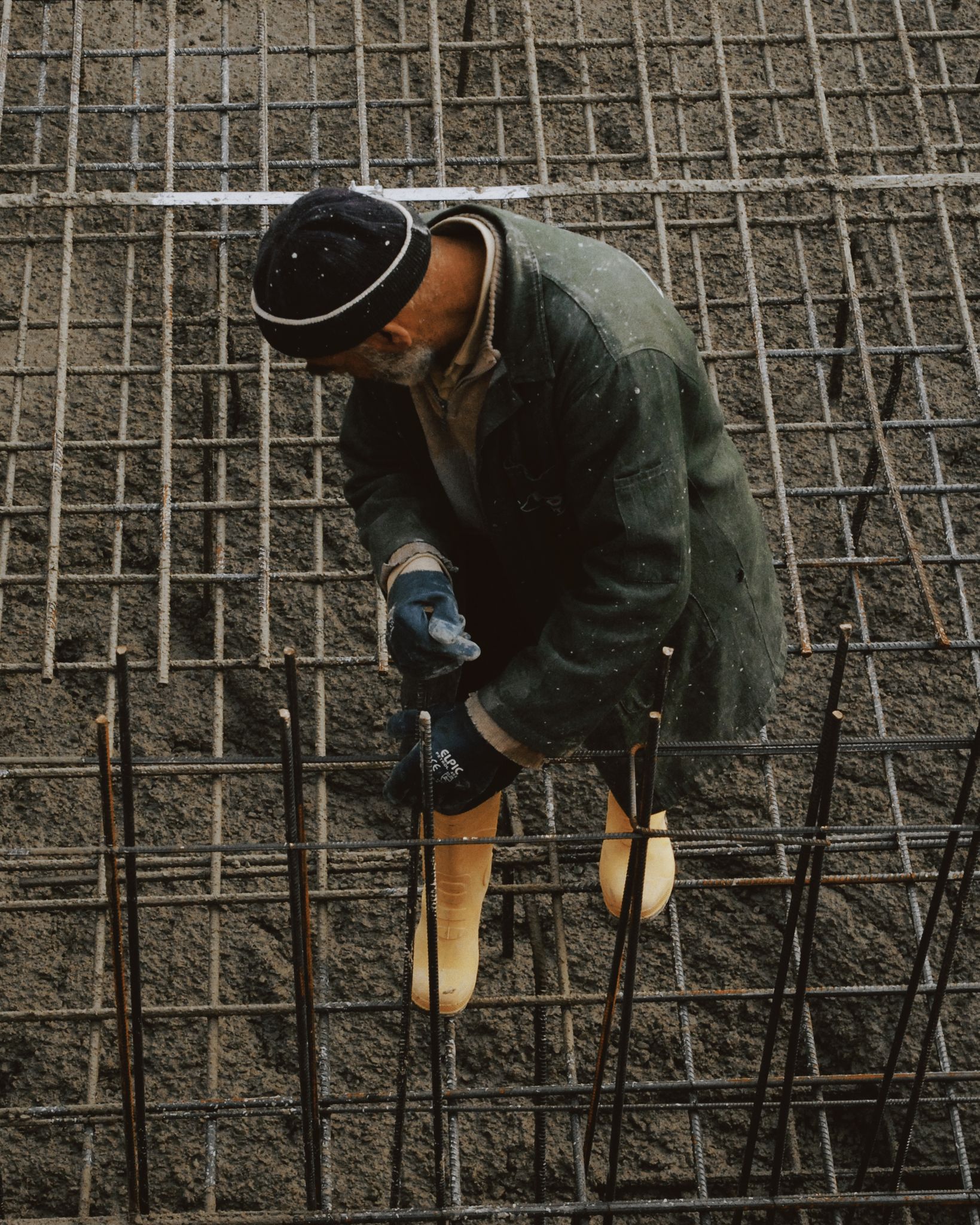 Construction worker in protective gear securing steel reinforcement bars at a building site.