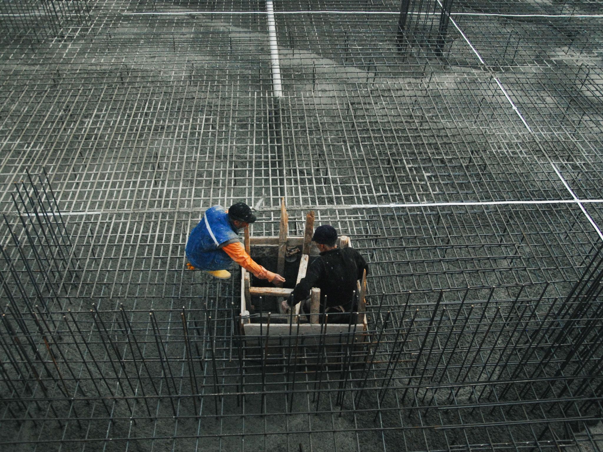 Two workers operating on a construction site with steel frameworks and concrete. High-angle view captures teamwork and industry.